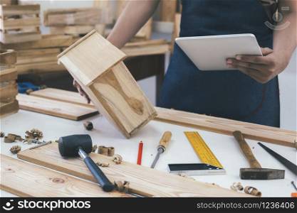 DIY woodworking and furniture making and craftsmanship and handwork concept. Carpenter working on woodworking machines in carpentry shop. Young man working as carpenter and taking wood stock.
