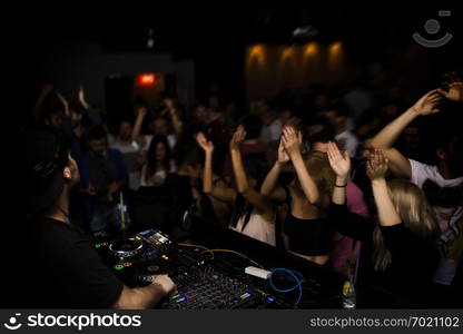 DJ and dj set at night club party. People at the party are having fun on the background.