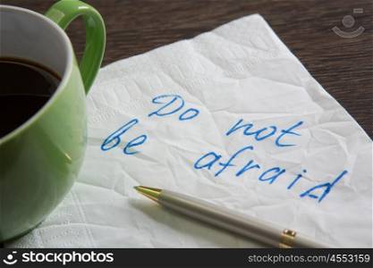 Do not be afraid. Message written on napkin and coffee cup on wooden napkin