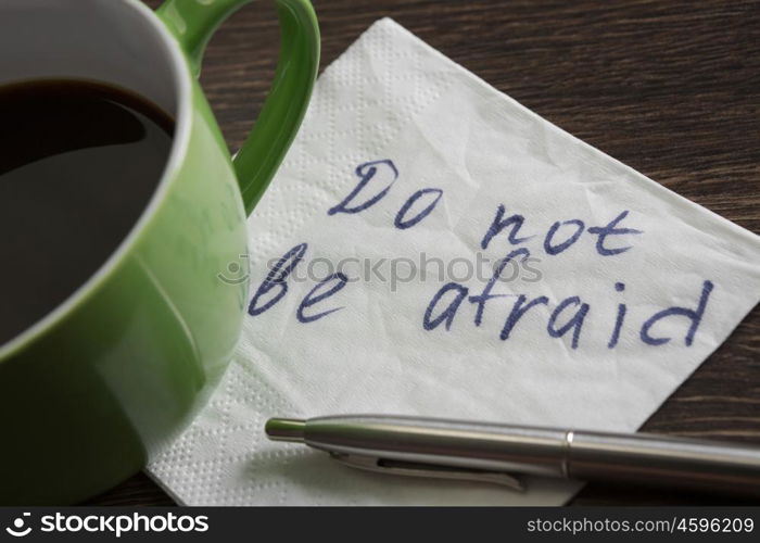 Do not be afraid. Message written on napkin and coffee cup on wooden napkin