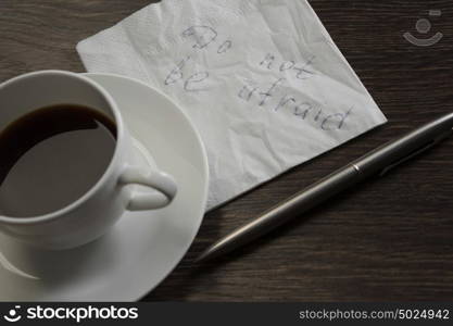 Do not be afraid. Message written on napkin and coffee cup on wooden napkin