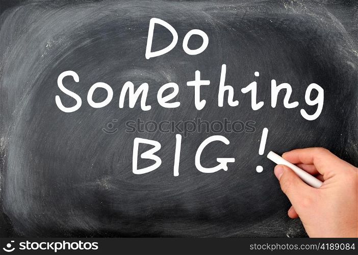 Do something big written with chalk on a blackboard background, with a hand holding chalk