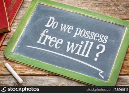 Do we possess free? A question in white chalk on a vintage blackboard with a stack of books against rustic wooden table
