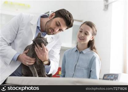 Doctor and girl checking cat on bed at veterinary clinic