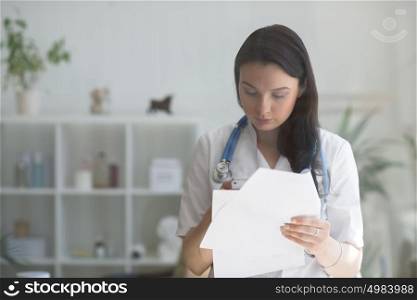 Doctor at her medical office using mobile phone and holding papers. View through the glass