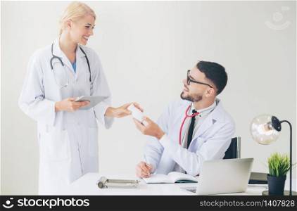 Doctor at hospital office passing medicine bottle to another doctor while having discussion about patients referral.. Doctor at hospital passes medicine to partner.