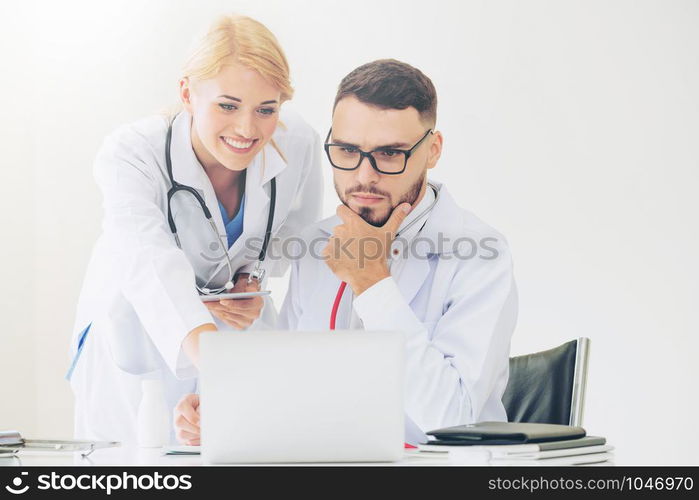 Doctor at hospital office working on laptop computer on the table with another doctor having discussion about patients health.