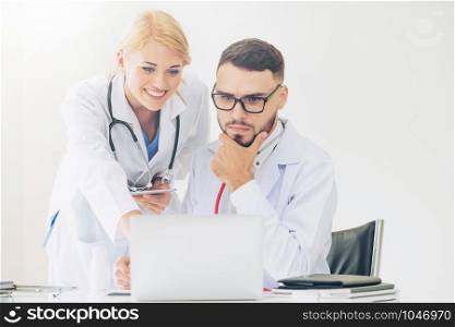 Doctor at hospital office working on laptop computer on the table with another doctor having discussion about patients health.