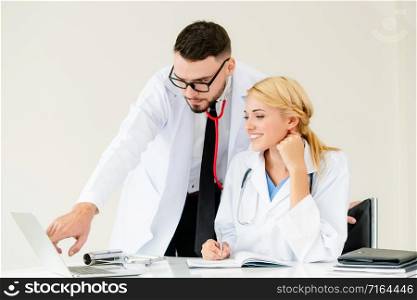 Doctor at hospital office working on laptop computer on the table with another doctor having discussion about patients health.. Doctor at hospital works on computer with partner.