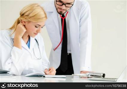 Doctor at hospital office writes notes on patients report while having conversation with another doctor that standing beside her.