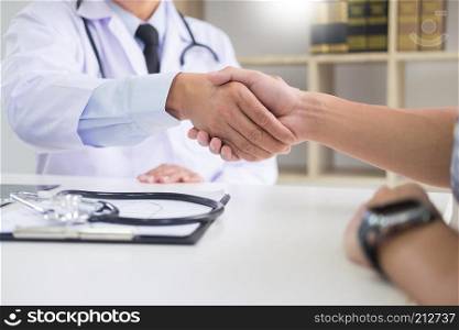 doctor at the clinic giving an handshake to his patient for encouragement and empathy, healthcare and assistance concept