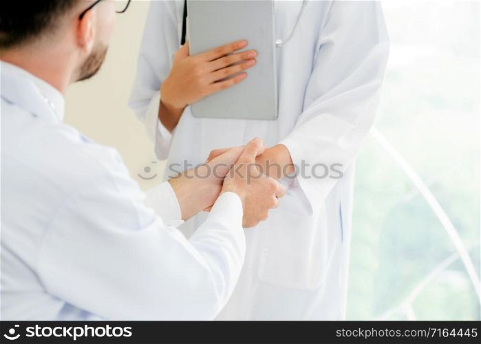Doctor at the hospital giving handshake to another doctor showing success and teamwork of professional healthcare staff.. Doctor at hospital shakes hand with another doctor