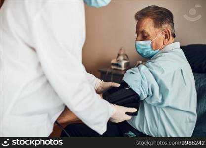 Doctor carying out blood pressure test and heart rate of senior man. Checking health condition elder patient suffering from arterial hypertension