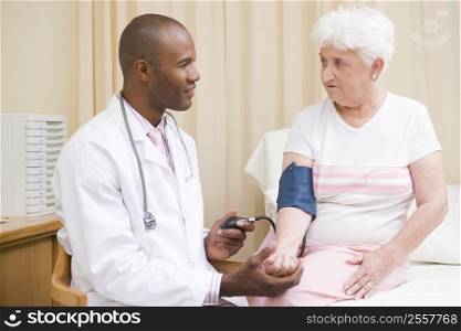 Doctor checking woman&acute;s blood pressure in exam room