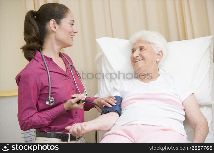 Doctor checking woman&acute;s blood pressure in exam room smiling