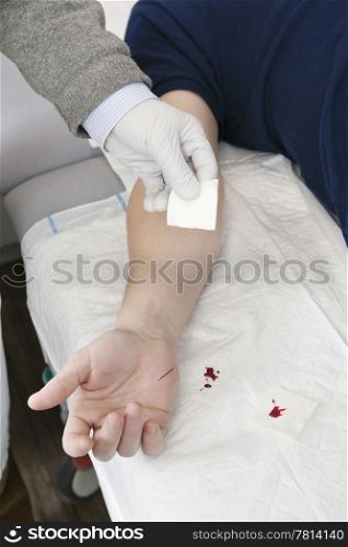 Doctor cleaning the cut on a patient&rsquo;s hand with a piece of gauze