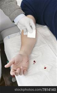 Doctor cleaning the cut on a patient&rsquo;s hand with a piece of gauze