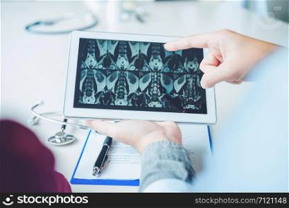 Doctor consulting with patient presenting x-ray film results on digital tablet tablet sitting at table