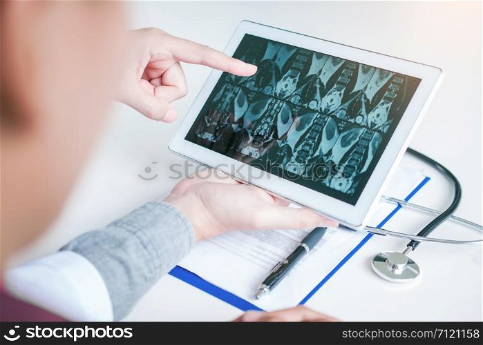 Doctor consulting with patient presenting x-ray film results on digital tablet tablet sitting at table