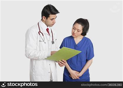 Doctor discussing medical report with female nurse over gray background