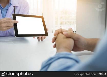 Doctor discussing patient notes in an office pointing to a clipboard with tablet as they make a diagnosis or decide on treatment
