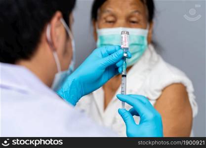 doctor draws medication out of vial before injection with syringe to senior patient and wearing a medical mask. Covid-19 or coronavirus vaccine