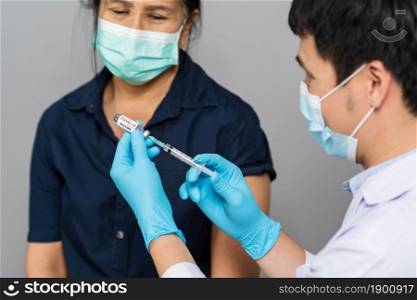 doctor draws medication out of vial before injection with syringe to woman and wearing a medical mask. Covid-19 or coronavirus vaccine