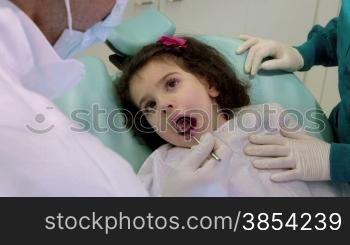 Doctor during visit of female child in dental clinic, dentist working with assistant, checking teeth of young baby girl. Sequence