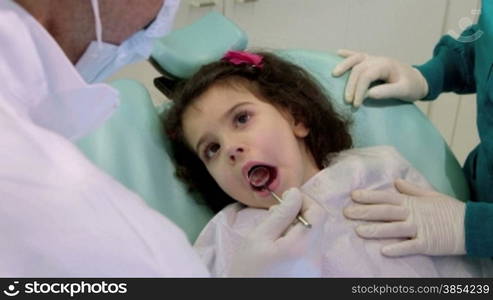 Doctor during visit of female child in dental clinic, dentist working with assistant, checking teeth of young baby girl. Sequence