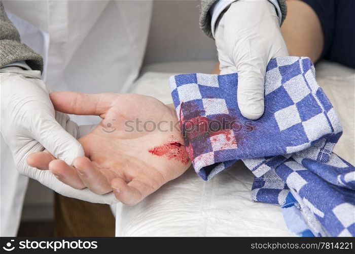 Doctor, examining a severe bleeding cut in the palm of a patient&rsquo;s hand