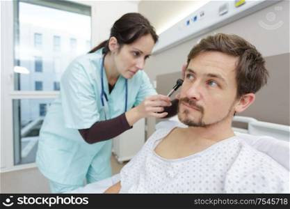doctor examining patients inner ear in hospital bed