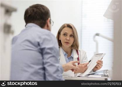 Doctor explaining prescription on clipboard to patient at desk in hospital