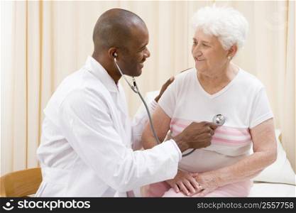 Doctor giving checkup with stethoscope to woman in exam room smiling