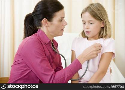 Doctor giving checkup with stethoscope to young girl in exam room