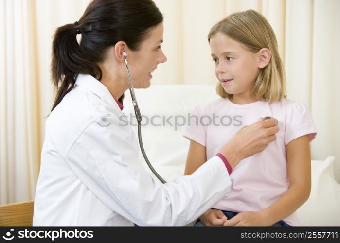 Doctor giving checkup with stethoscope to young girl in exam room