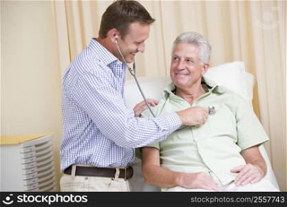 Doctor giving man checkup with stethoscope in exam room smiling
