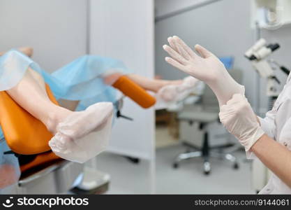 Doctor gynecologist wearing sterile rubber preparing for woman examination on chair. Female checkup in gynecological cabinet. Doctor gynecologist wearing sterile rubber preparing for examination