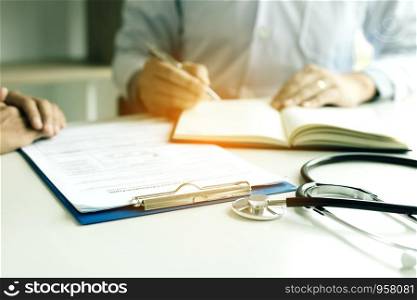 Doctor hand holding pen writing patient history list on note pad and talking to the patient about medication and treatment.