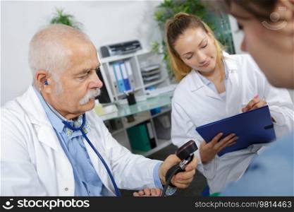 Doctor holding blood pressure gauge, assistant taking notes