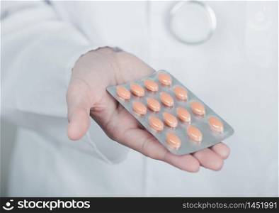 Doctor holding strip of pills on light hospital wall background. Antibiotics, vitamins and virus treatment tablet.