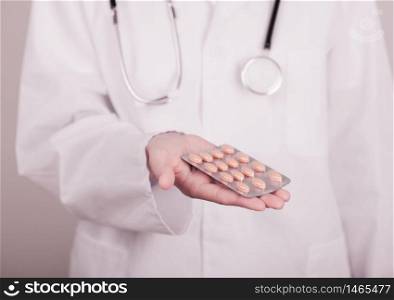 Doctor holding strip of pills on light hospital wall background. Antibiotics, vitamins and virus treatment tablet.