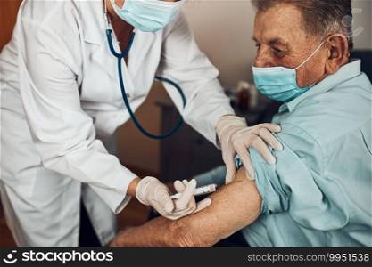 Doctor holding syringe with vaccine and making injection to senior patient with medical mask. Covid-19 or coronavirus vaccine. Physician wearing white coat and gloves using face mask