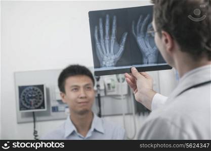 Doctor holding up and looking at x-ray of patients hand bones, patient in the background