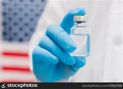 Doctor holding vaccine bottle with USA flag background.