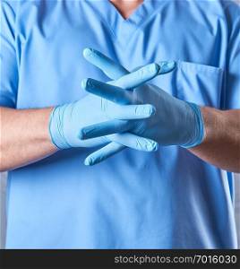 doctor in a blue uniform puts on sterile latex gloves, close up