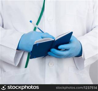 doctor in a white coat and blue gloves holds a blue paper notebook for notes, stethoscope hangs on his neck, white medical backdrop, close up