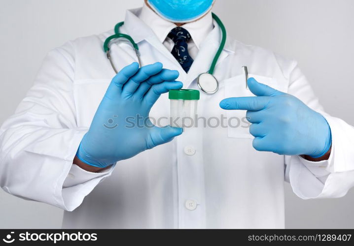 doctor in a white coat and blue sterile latex gloves holds a plastic jar for stool analysis, white background