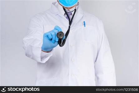 doctor in a white coat and tie holds in his hand a black phonendoscope, wearing blue sterile gloves, white background