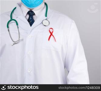 doctor in a white coat and tie is standing on a white background, red silk ribbon is hanging on his chest, symbol of the fight against disease AID