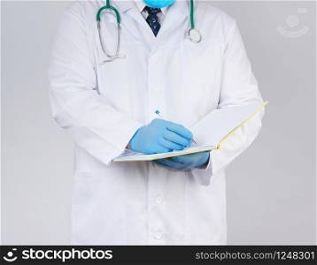 doctor in a white coat, blue latex sterile gloves holds an open yellow notebook in his hand on a white background, concept of recording the diagnosis when visiting patients